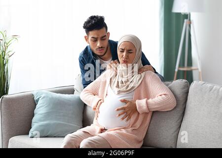 Contrazioni di manodopera. Preoccupatevi marito che fa massaggio alla sua moglie musulmana incinta Foto Stock