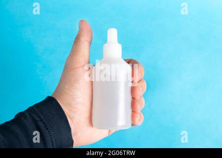 l'uomo tiene in mano la bottiglia trasparente di antisettico. La bottiglia dell'igienizzatore in mano maschile su sfondo blu. Spazio di copia per testo o disegno. Foto Stock