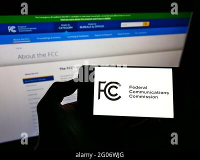 Persona in possesso di smartphone con sigillo della Federal Communications Commission (FCC) dell'agenzia statunitense sullo schermo davanti al sito Web. Mettere a fuoco il display del telefono. Foto Stock