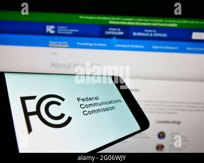 Telefono cellulare con sigillo della Federal Communications Commission (FCC) dell'agenzia statunitense sullo schermo davanti alla pagina web. Mettere a fuoco il centro-destra del display del telefono. Foto Stock