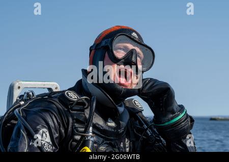 17 aprile 2021 - Hamburgsund, Svezia: Un subacqueo in attesa che la barca da immersione entri in posizione in modo da poter entrare in acqua. Oceano e cielo blu sullo sfondo Foto Stock