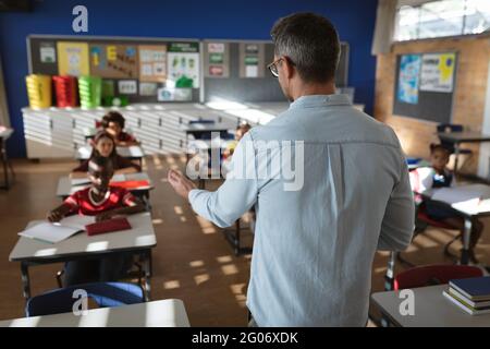 Vista posteriore dell'insegnamento di insegnanti maschi caucasici a diversi studenti della classe elementare Foto Stock