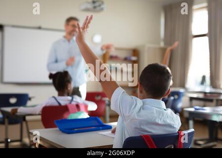 Gruppo di studenti diversi che alzano le mani nella classe delle scuole elementari Foto Stock