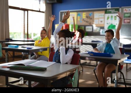 Gruppo di studenti diversi che alzano le mani nella classe delle scuole elementari Foto Stock