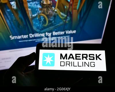 Persona che tiene il cellulare con il logo della società danese di giacimenti petroliferi Maersk perforazione COME sullo schermo di fronte alla pagina web aziendale. Mettere a fuoco il display del telefono. Foto Stock