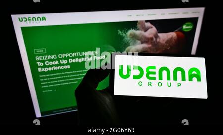 Persona che detiene il cellulare con il logo aziendale del conglomerato filippino Udenna Corporation sullo schermo davanti alla pagina web. Mettere a fuoco il display del telefono. Foto Stock