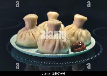 Khinkali deliziosi gnocchi georgiani su un piatto blu con forte adjika su sfondo nero Foto Stock