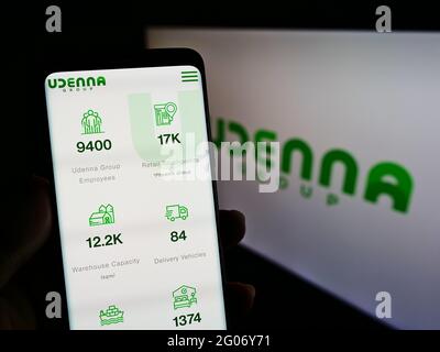 Persona titolare smartphone con sito web del conglomerato filippino Udenna Corporation sullo schermo davanti al logo. Mettere a fuoco il centro del display del telefono. Foto Stock