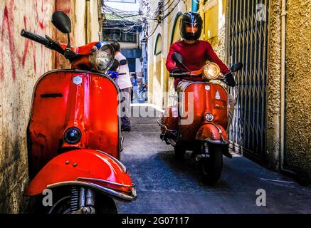 Un giovane maschio su uno scooter rosso Vespa viaggia lungo un vicolo stretto a Chinatown, Bangkok, Thailandia. Foto Stock