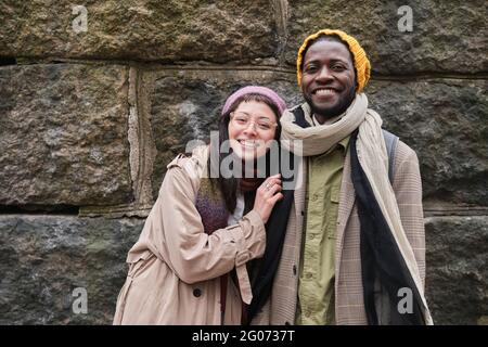 Ritratto di felice giovane coppia in abiti caldi sorridente a macchina fotografica in piedi in città Foto Stock