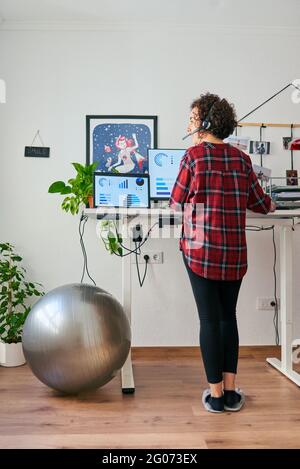 Donna che telelavoro su una scrivania regolabile in piedi accanto a a. montare la sfera Foto Stock