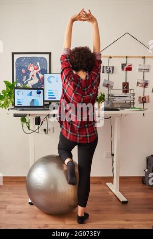 Donna che telelavoro su una scrivania regolabile in piedi accanto a a. montare la sfera Foto Stock