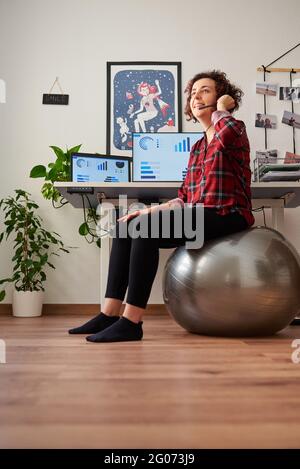 Donna che lavora in telelavoro seduto su un flipper di fronte a lei parlare in scrivania con un auricolare Foto Stock