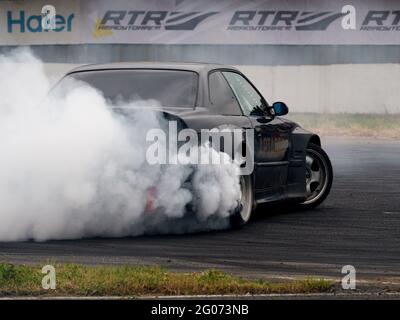 Fumo visto da sotto le ruote di un'auto da corsa, durante l'evento.Festival Drift Expo Track Mode si svolge il 29-30 maggio presso ADM Raceway con la mostra di progetti modificati per il drifting come; ‘DRift Taxi’ - un’opportunità per viaggiare come passeggero con un pilota professionista in una vettura sportiva appositamente preparata sulla pista da corsa, ‘DRift Trike Area’ - una piattaforma dove si può provare a guidare un vero e proprio trike di deriva e ‘RC Drift’ - deriva su auto radiocomandate. Foto Stock