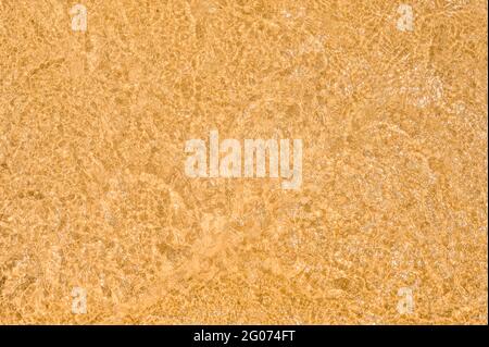 la sabbia dorata è visibile attraverso l'acqua limpida del mare. Spiaggia sabbia mare acqua sfondo estivo. Schiuma bianca onda sabbia fine Foto Stock