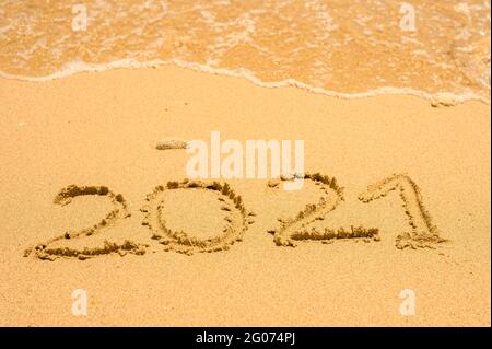 Immagine closeup di 2021 numeri che vengono lavati dalla sabbia bagnata sulla spiaggia dall'onda del mare. Concetto di suumer di viaggio 2021 Foto Stock