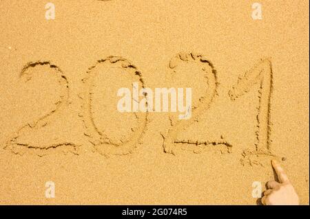 Testo scritto a mano 2021 sulla sabbia bagnata dorata sulla spiaggia. Recupero dopo covid-19 concetto e viaggio di felicità Foto Stock