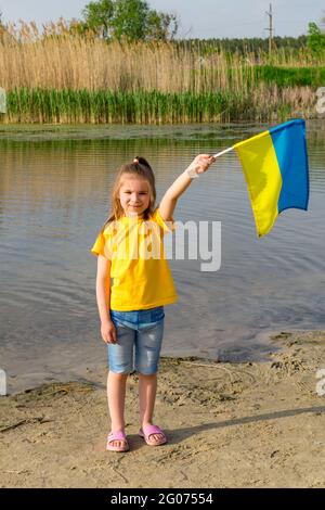 La bandiera dell'Ucraina sta volando nelle mani di una bambina Ucraina sullo sfondo di un lago e canne. Giornata dell'indipendenza dell'Ucraina e bandiera Foto Stock