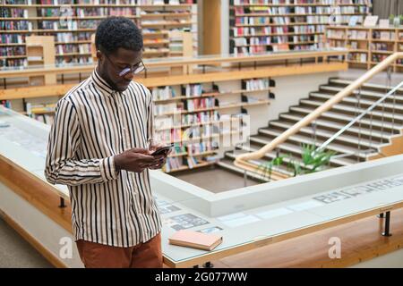 Giovane africano che usa il telefono cellulare mentre si trova in biblioteca Foto Stock