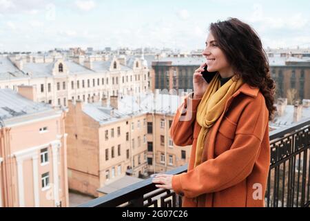 Giovane donna in abiti caldi che parla sul telefono cellulare mentre si guarda una bella vista all'aperto Foto Stock