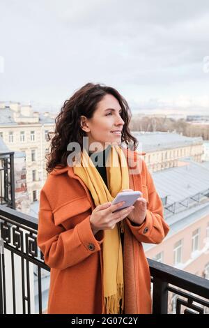 Giovane donna sorridente che usa il suo telefono cellulare mentre si alza in piedi all'aperto Foto Stock