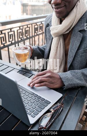Primo piano di uomo d'affari seduto al tavolo con il tè e lavorando online in caffetteria Foto Stock