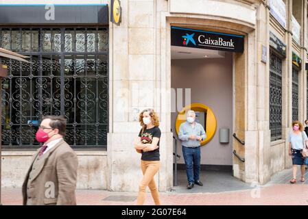 Le persone che indossano mascherine come precauzione contro la diffusione del covid-19 a piedi oltre il ramo della banca la Caixa. Foto Stock