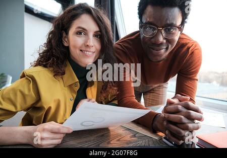 Ritratto dei colleghi che sorridono alla fotocamera mentre lavorano con i documenti al tavolo Foto Stock