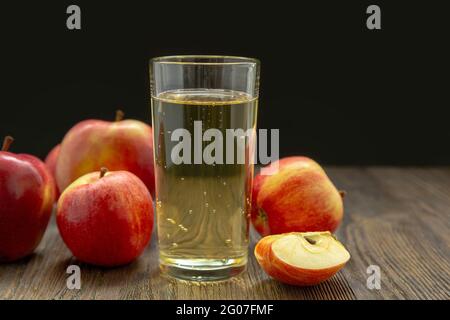 Sidro di mela duro in un bicchiere e mele rosse mature su sfondo nero Foto Stock