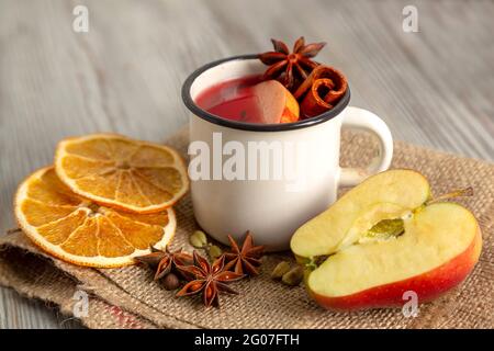 VIN brulé in tazza bianca con frutta e spezie su fondo ligneo. Tradizionale bevanda calda natalizia con vino rosso, mele, arance, anice Foto Stock