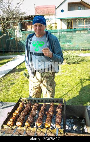 Picnic in natura. Un uomo sta grigliando i kebab marinati. Primo piano foto di kebab caucasici nel giardino cottage. Foto Stock