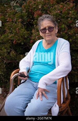 Una donna di 85 anni, indossando occhiali, seduta su una sedia. Foto Stock