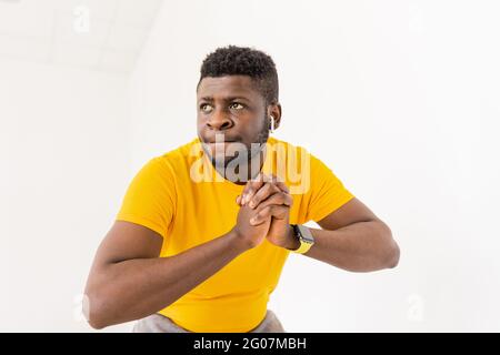 Concentrato giovane afroamericano in giallo trendy t-shirt, facendo esercizi squat, fitness workout. Il ragazzo nero sportivo si è concentrato sul miglioramento di sé Foto Stock