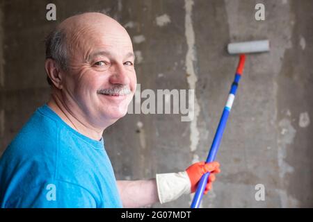 L'uomo dipinge le pareti di cemento usando la spazzola a rullo e il primer facendo un rinnovamento. Foto Stock