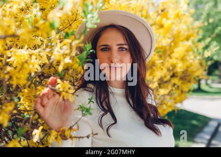 Ritratto di giovane donna di mezza età in posa in giardino fiorente primavera. Elegante donna circondata da fiori guarda la macchina fotografica Foto Stock