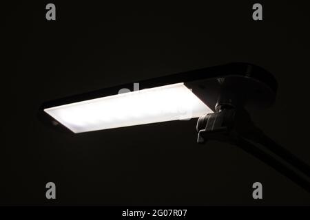 La lampada fluorescente da tavolo risplende al buio da vicino Foto Stock