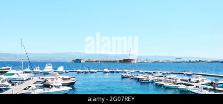 Messina, Sicilia, Italia - 26 aprile 2021: Porto di Messina con barche ormeggiate, statua dorata della Madonna della Lettera e costa calabrese sullo sfondo. Foto Stock