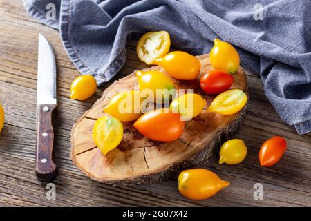vari pomodori maturi colorati su sfondo di legno. Cottura con pomodoro giallo arancio e rosso ciliegia con coltello Foto Stock