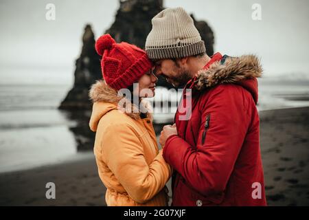 Vista laterale di giovane uomo e donna in inverno indossare in piedi sulla costa vicino a grandi pietre e acqua Foto Stock