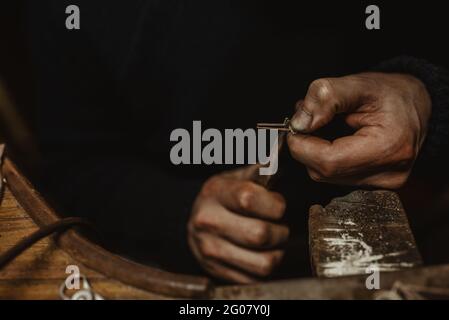 Orafo maschio con cuscinetti che usano pinze mentre fanno piccoli dettagli di metallo sul banco di lavoro in officina Foto Stock