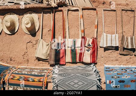 Stuoie colorate fatte a mano borse e cappelli di paglia su pietra marrone Muro sulla strada in Marocco Foto Stock