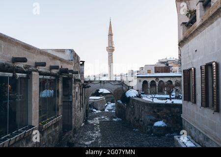 Strada vuota con pietre di pavimentazione che conduce tra gli edifici antichi a. Alta torre minareto contro il cielo blu chiaro in Turchia in periodo invernale Foto Stock