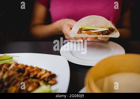 Mani di Donna seduto al tavolo da pranzo e tenendo pezzetto d'anatra di Pechino su pane piatto di riso su piatto di ceramica Foto Stock
