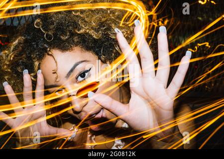 Giovane donna etnica espressiva con capelli afro in occhiali da sole eleganti e la parte superiore che tocca la testa e gridando ad alta voce mentre freddo dentro nightclub vicino al freeze Foto Stock
