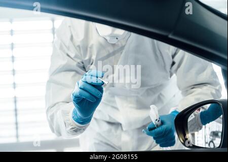 Biologo con guanti protettivi che esegue un test del coronavirus su un persona in auto Foto Stock