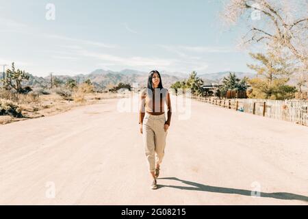 Corpo pieno di brunette che cammina lungo la strada vuota in caldo Terreno del Joshua Tree National Park in California USA Foto Stock