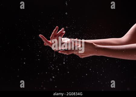 Vista rifilata di donna anonima lavando le mani con spruzzi d'acqua su sfondo nero Foto Stock