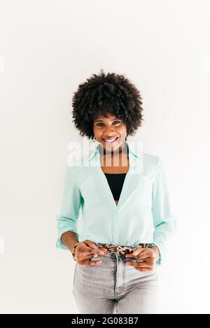 Felice giovane afroamericana femmina con bei capelli afro dentro outfit alla moda su sfondo bianco Foto Stock