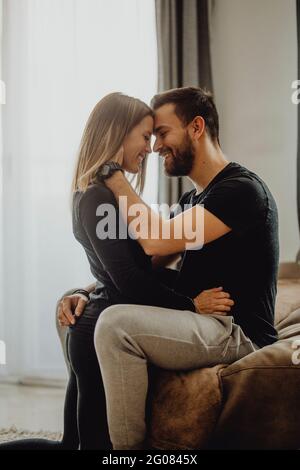 Sorridente femmina abbracciando e baciando l'uomo allegro in fronte mentre sedersi insieme su un comodo divano a casa Foto Stock