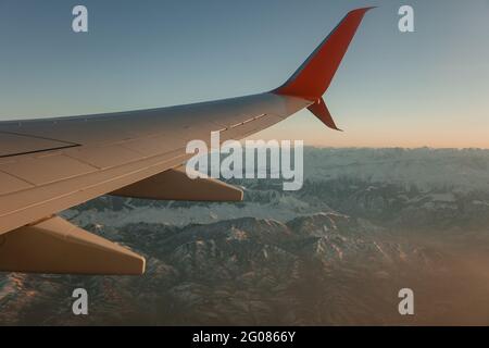 Primo piano dell'ala dell'aeroplano sopra le montagne innevate durante il volo Foto Stock
